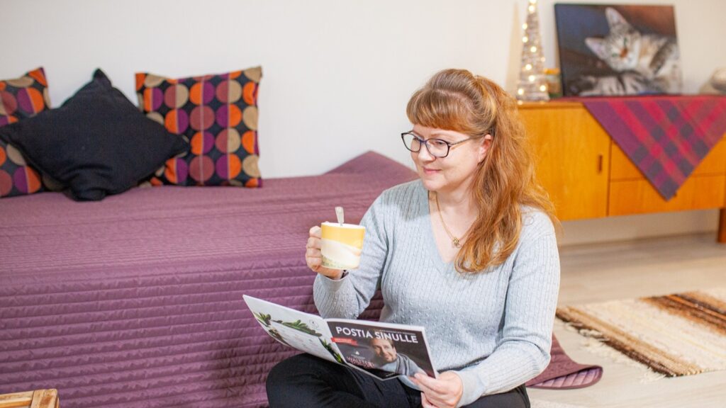 Nainen lukee lehteä makuuhuoneessa ja juo teetä
