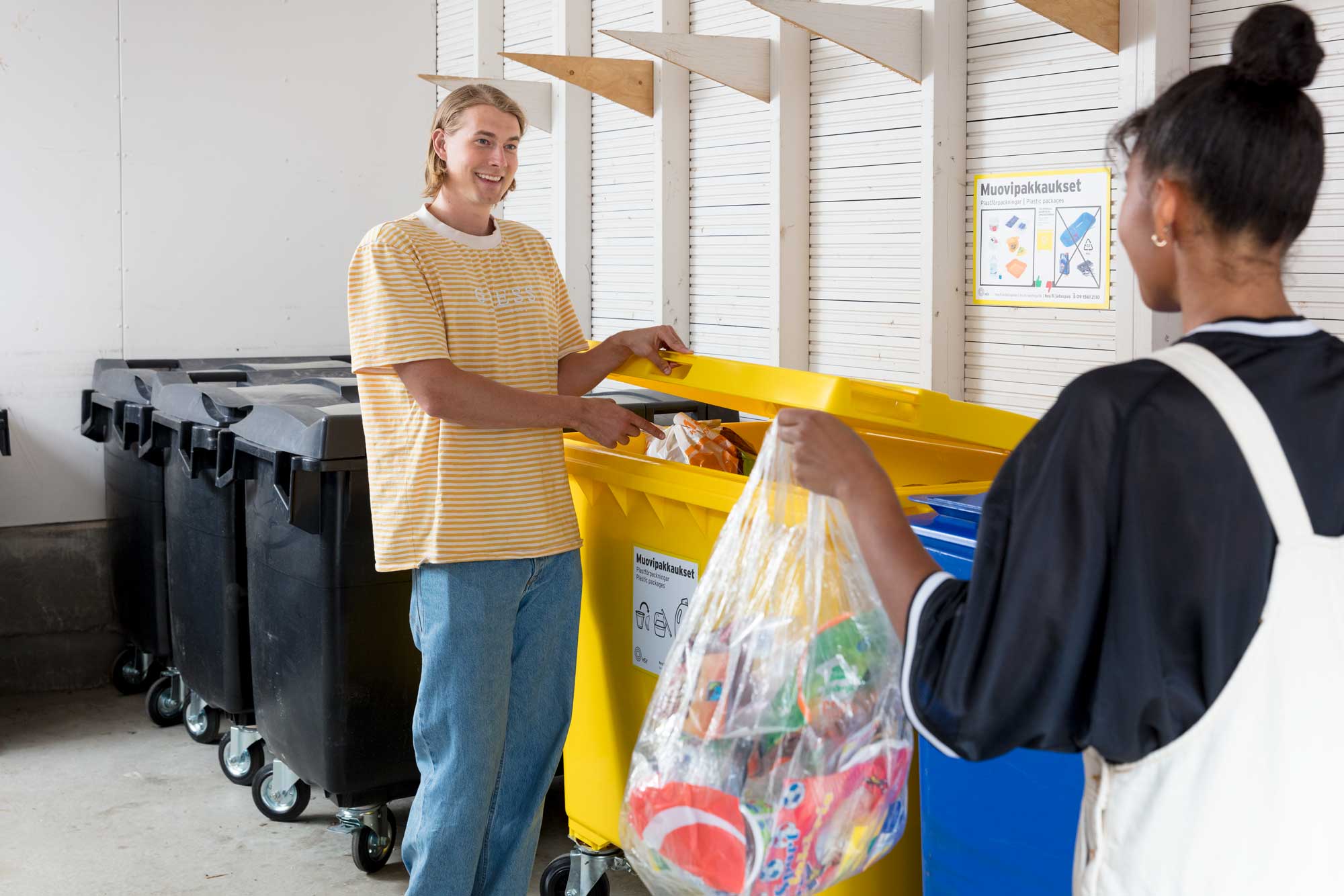 Kaksi henkilöä viemässä roskia jäteastiaan.